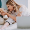 Lifestyle photo of woman on a bed with her dog and laptop